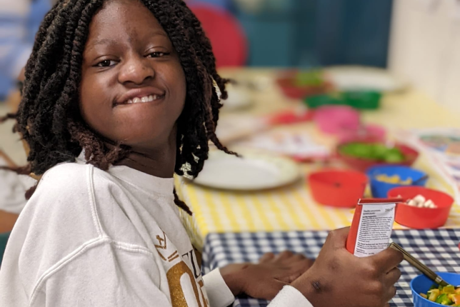 Young person smiling while holding a bottle of paint.