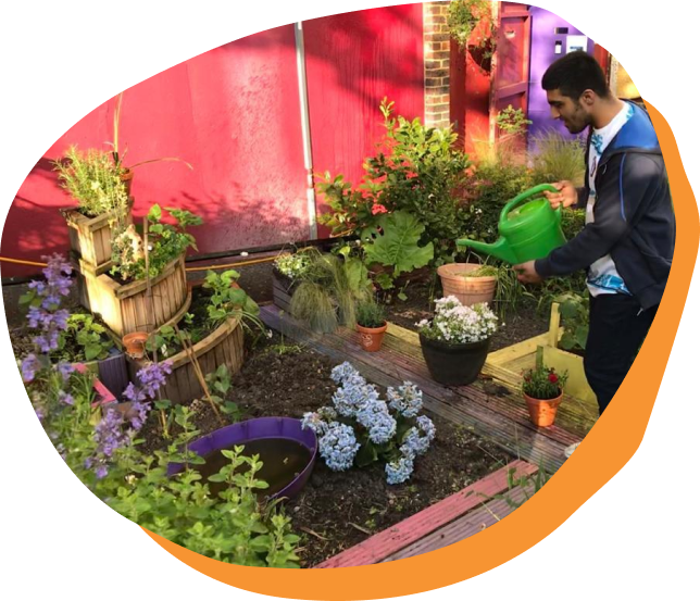 A young person watering a garden outside Caxton youth club.