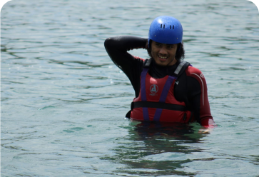 A young person in water wearing a blue helmet and a red life jacket.