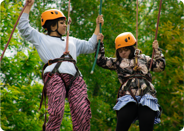 2 people wearing orange helmets holding on to ropes.