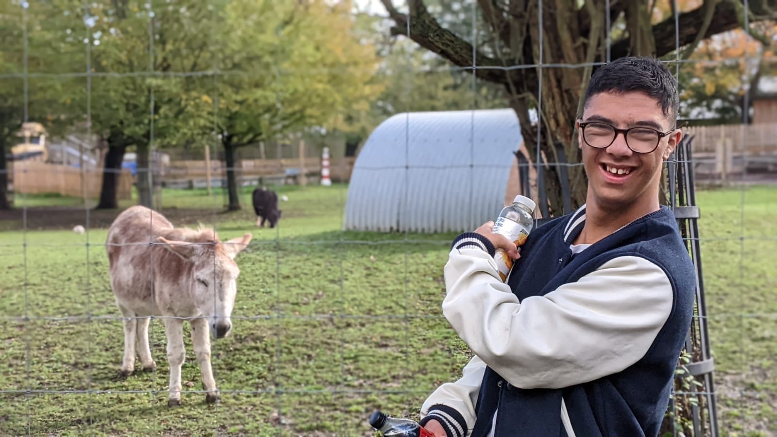 A young person smiling and pointing to a donkey standing behind him.