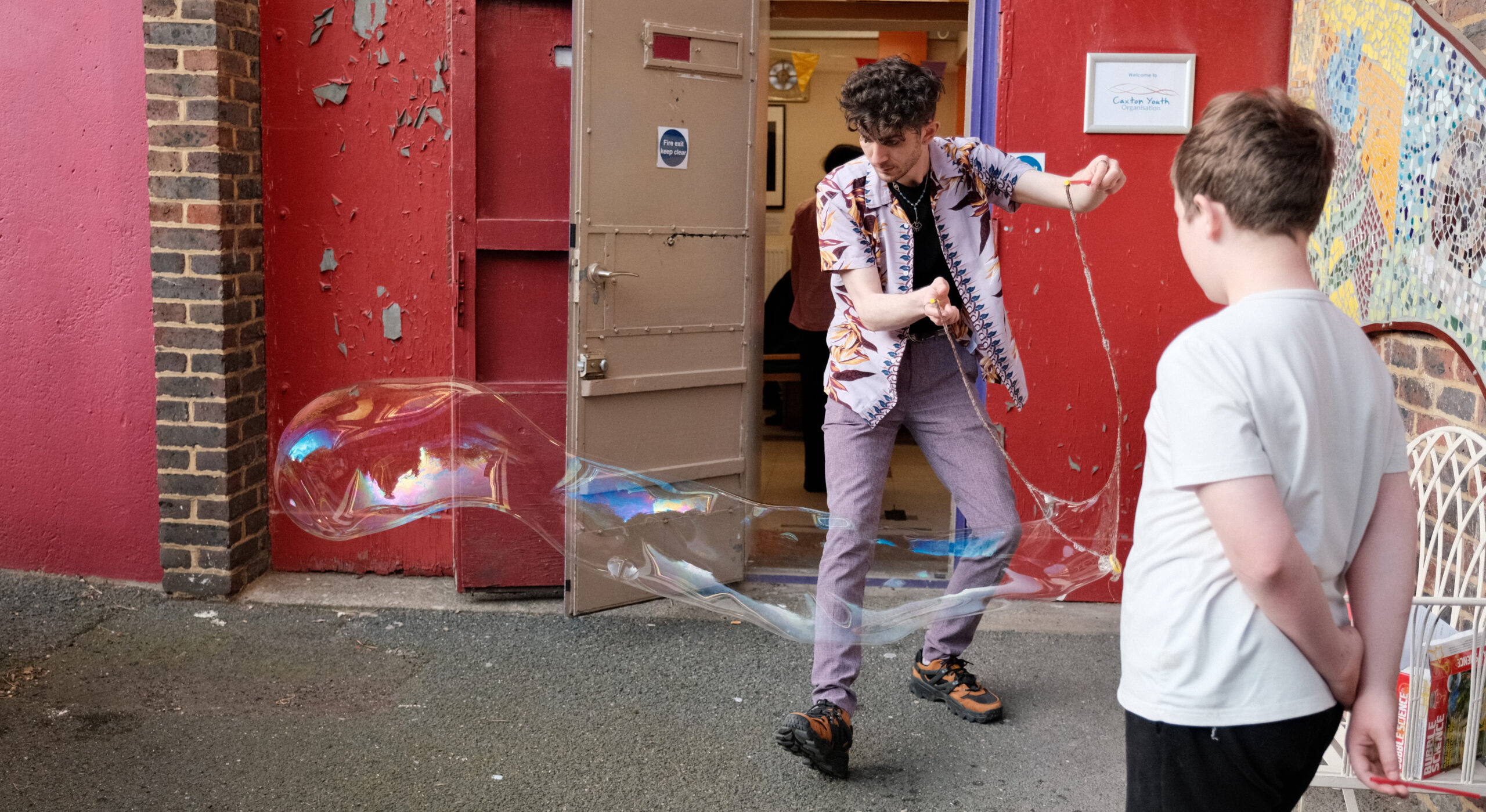 A young person and youth worker blowing bubbles outside Caxton youth club.