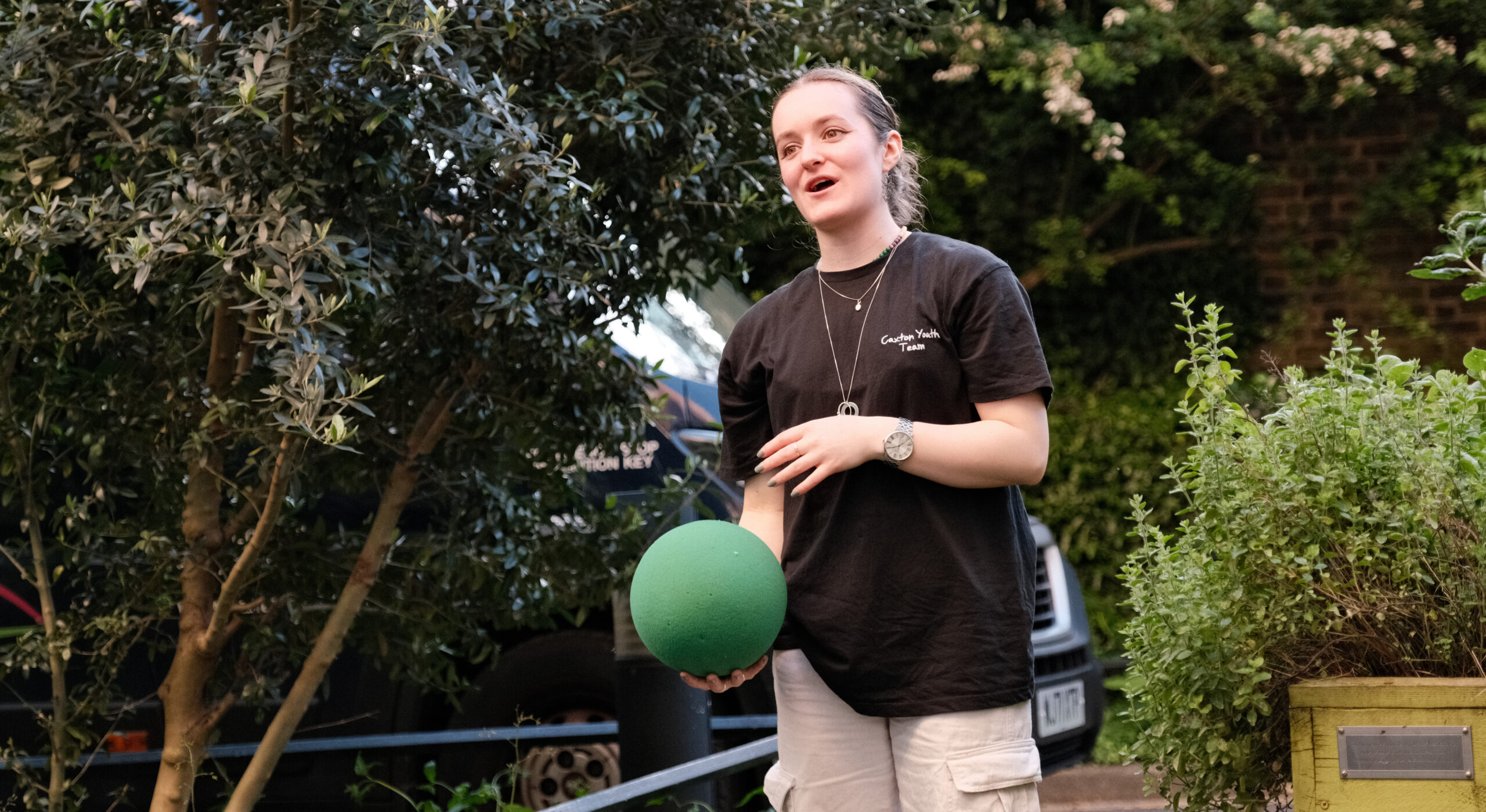 A person wearing a Caxton Youth uniform holding a green ball.