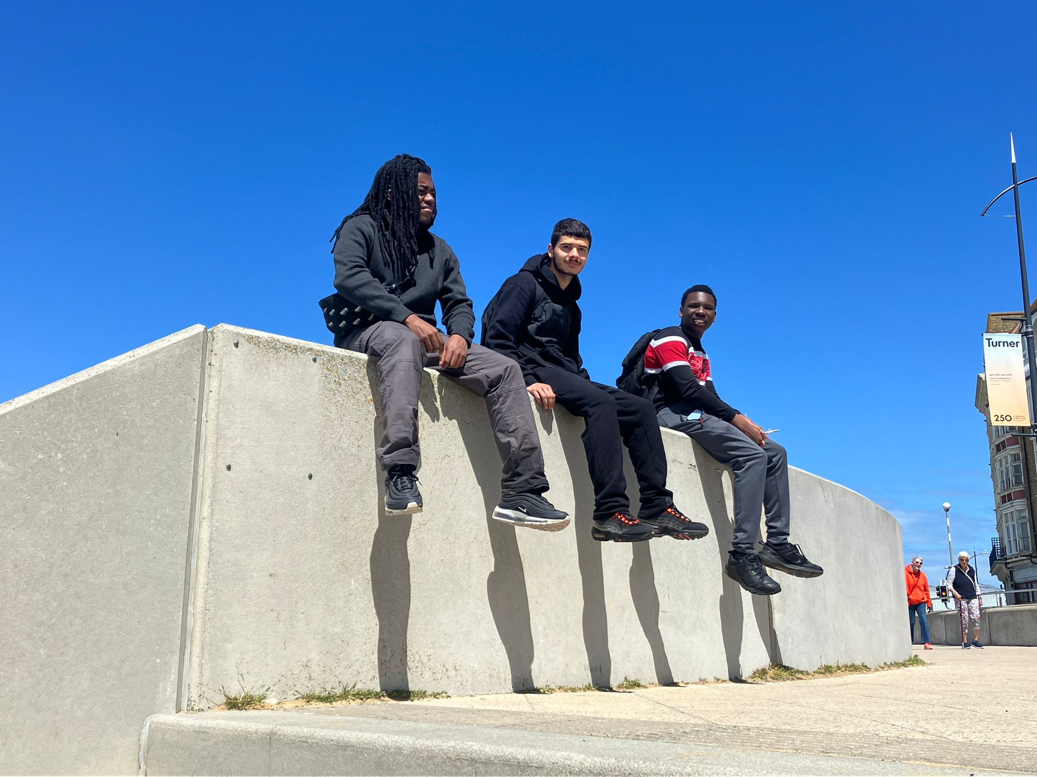 Three boys sitting on concrete. There is a blue sky behind them.