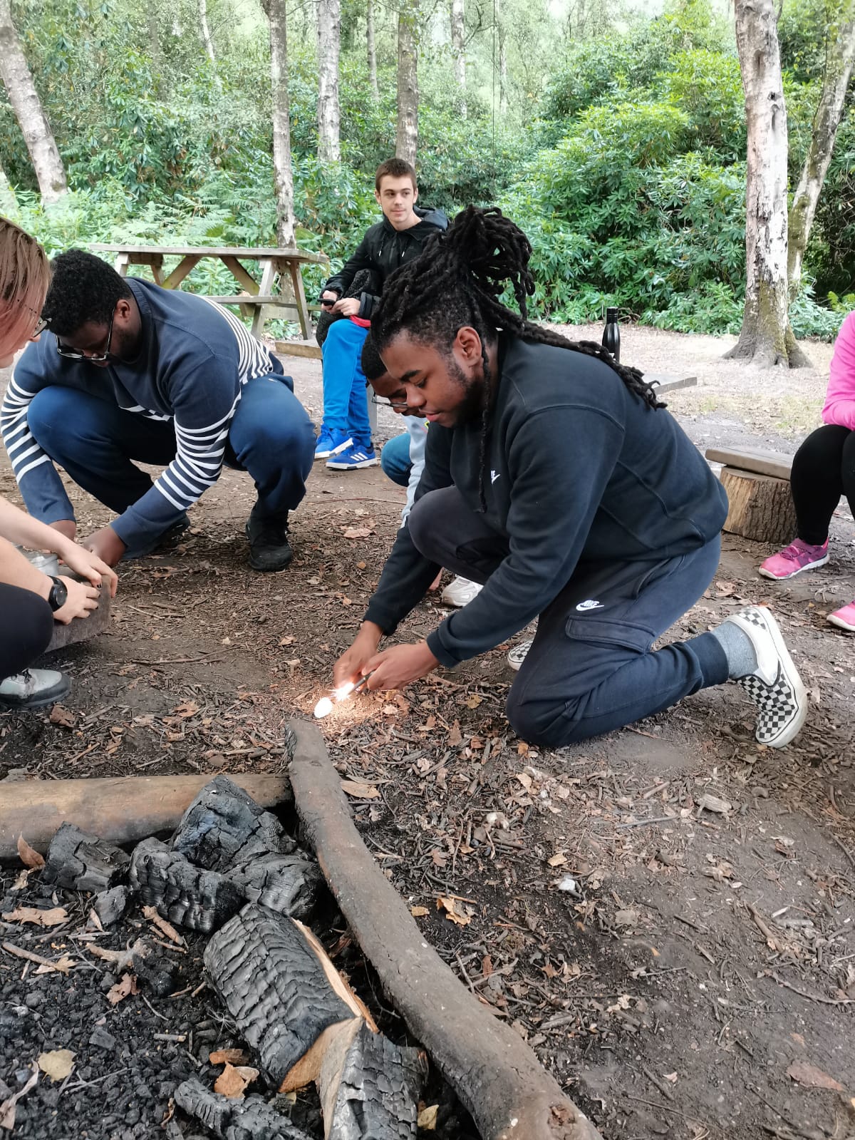 A young person wearing a navy tracksuit outdoors staring a fire